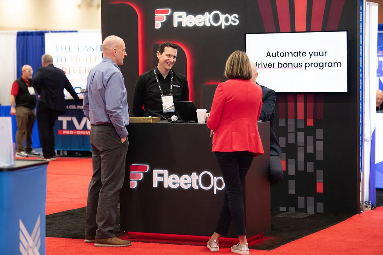 Two visitors talking with FleetOps staff across the counter of the FleetOps stand at a trucking trade show